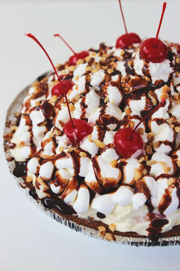 a pie in a chocolate cookie crust topped with bananas, peanuts, cherries, and chocolate syrup.