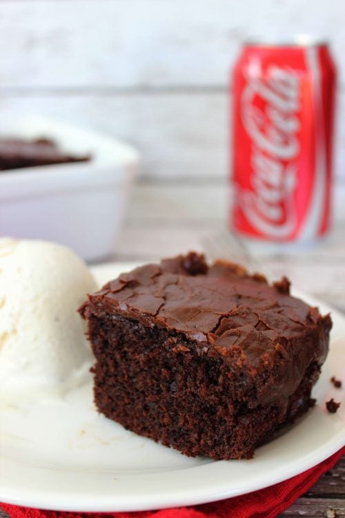 a slice of chocolate cake with chocolate frosting with a coca cola can in the background. 