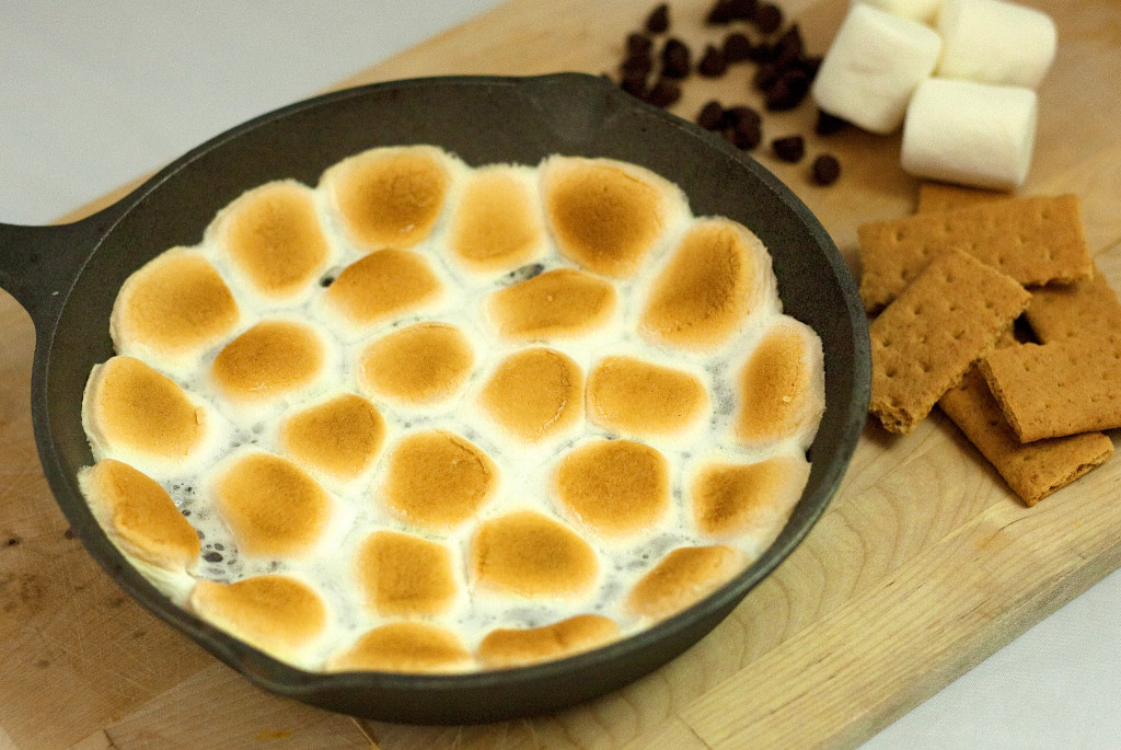 a cast iron skillet of smores dip topped with toasted marshmallows. 