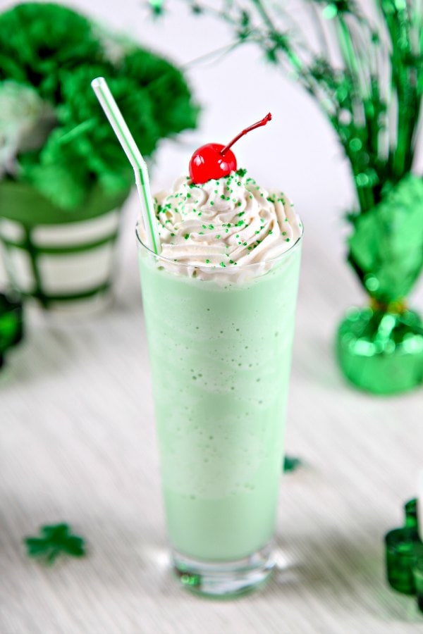 a green mint milkshake in a tall glass topped with whipped cream and a cherry. 