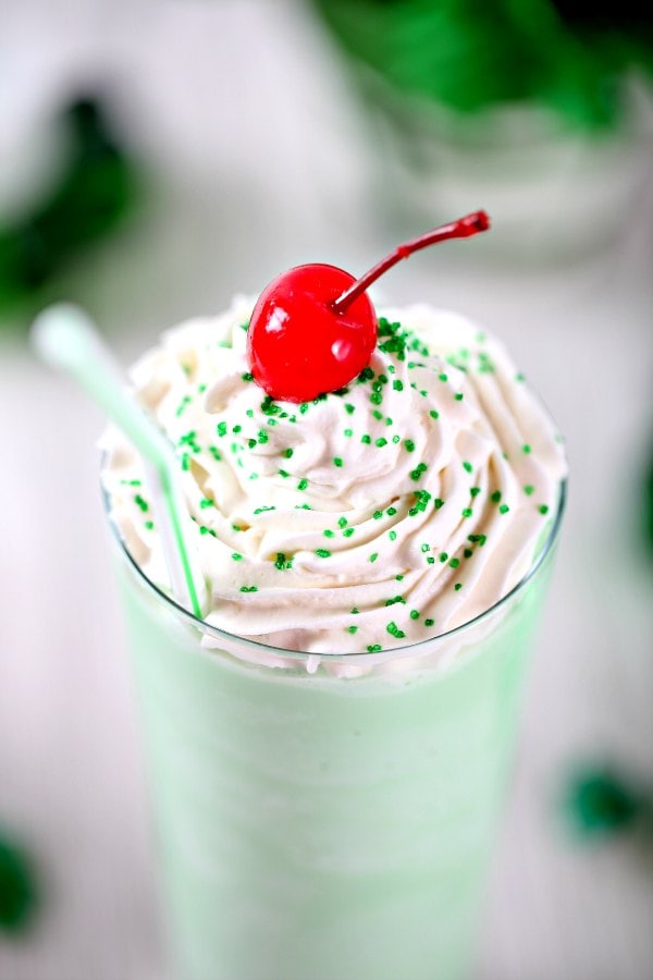 a closeup of a copycat shamrock shake topped with whipepd cream, green sprinkles, and a marachino cherry. 