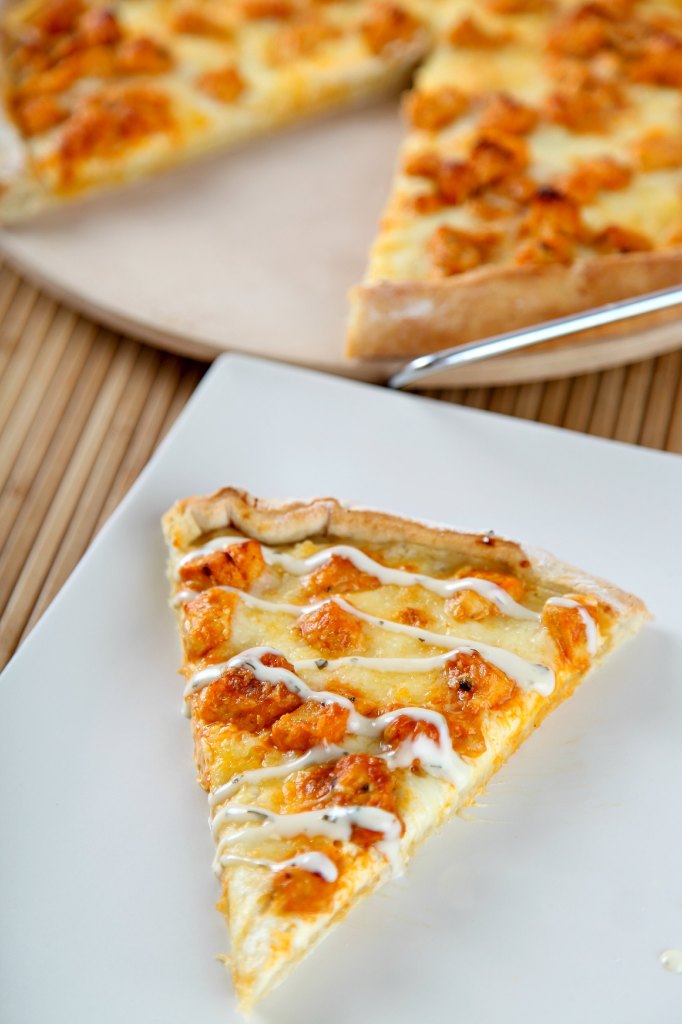 a slice of buffalo chicken pizza with a whole pizza in the background.