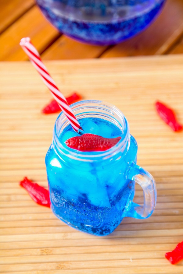 a glass mug filled with an ocean water drink topped with swedish fish and a red and white straw.