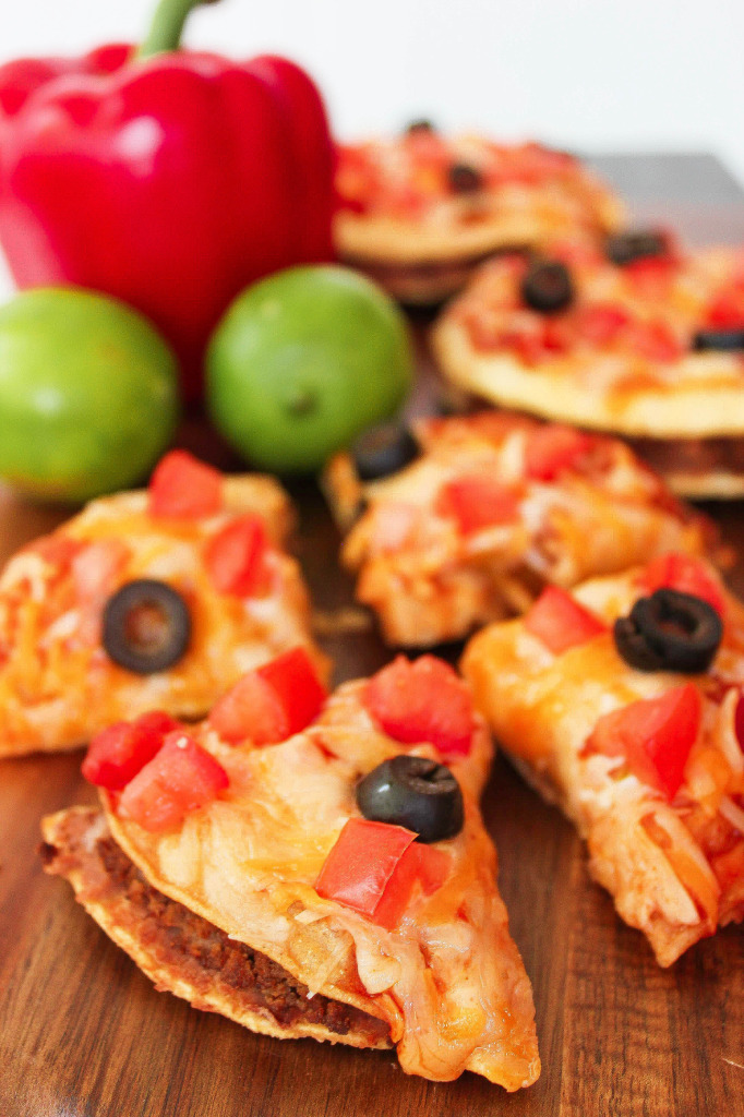 a mexican pizza cut into fourths and topped with cheese, tomatoes, and diced tomatoes. 