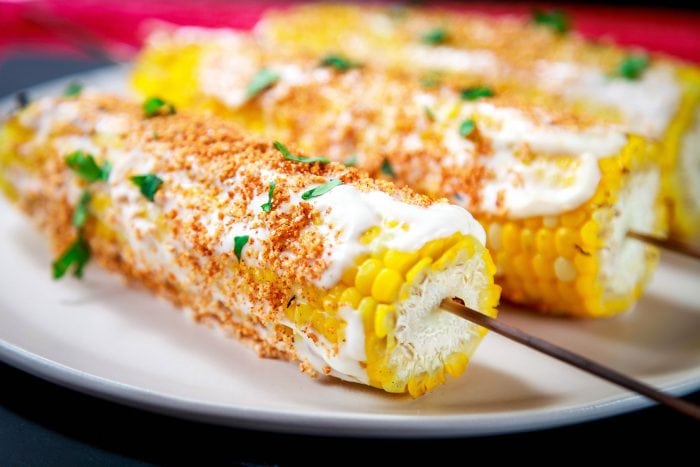 a closeup image of a mexican street corn topped with mayonnaise, chili powder, and parsley 