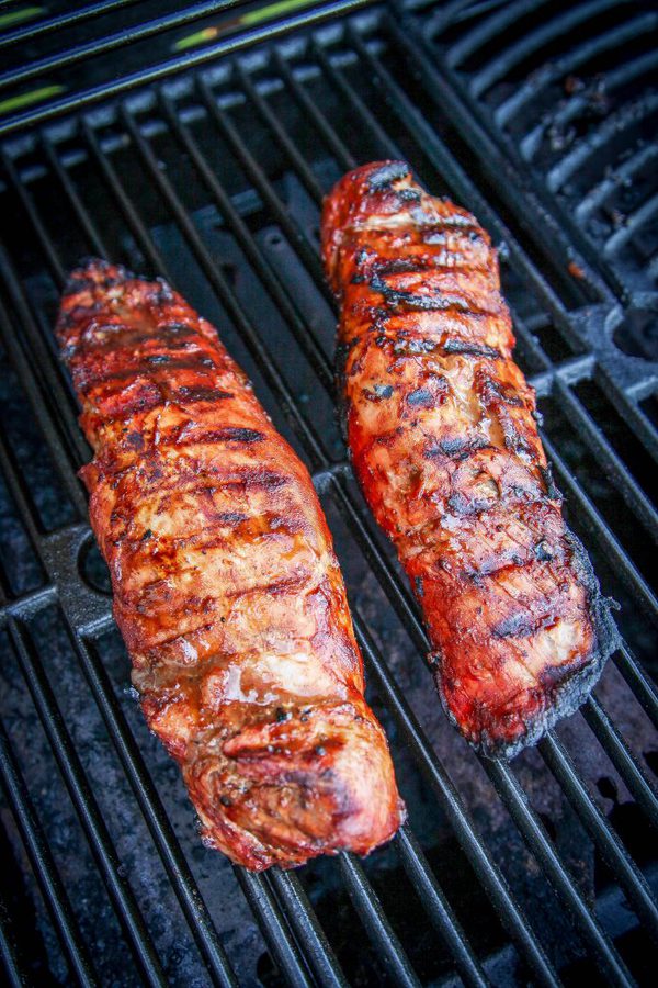 a sliced pork tenderloin brushed with BBQ sauce on a wooden cutting board.