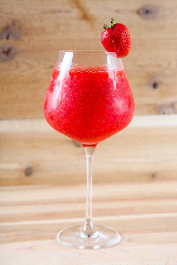a strawberry daiquiri in a wine glass garnished with a fresh strawberry. 