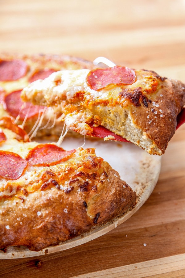 a red spatula lifting up a piece of pepperoni pretzel crust pizza.