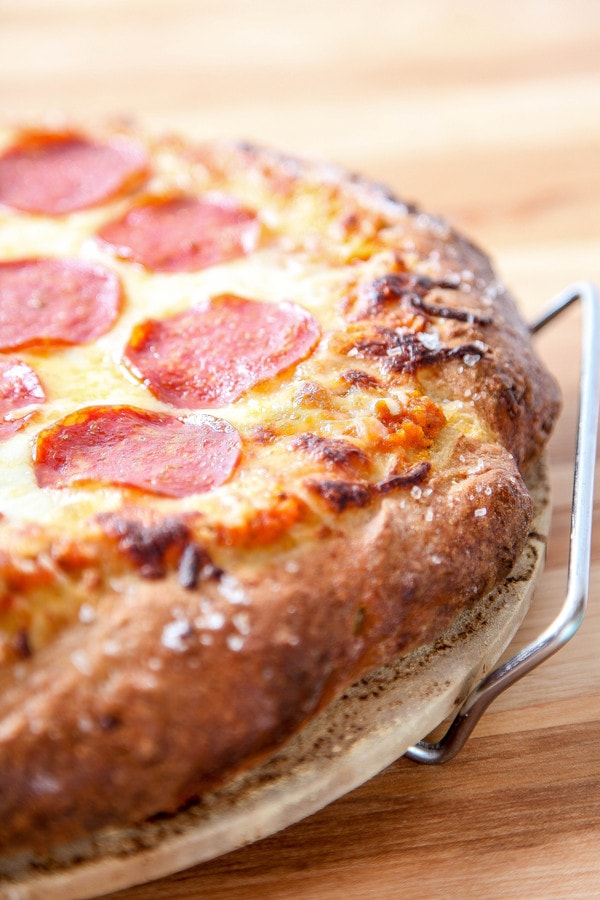 a pizza with flaky salt on the crust with pepperoni and cheese on a pizza stone. 