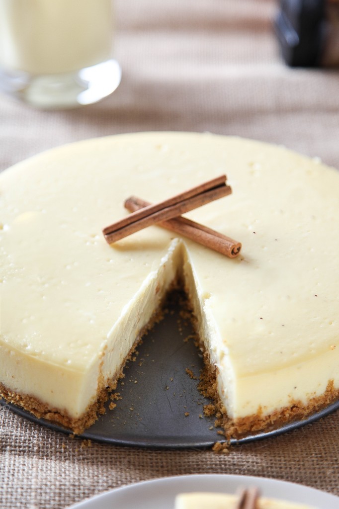 an eggnog cheesecake with a graham cracker crust with one slice cut out of it. 