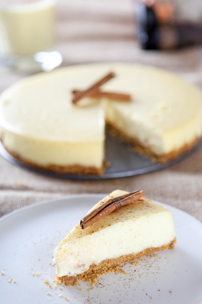 a slice of eggnog cheesecake with a graham cracker crust sprinkled with nutmeg and a cinnamon stick.