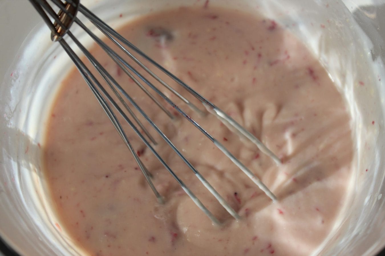 strawberries, milk, and pudding being mixed with a whisk.
