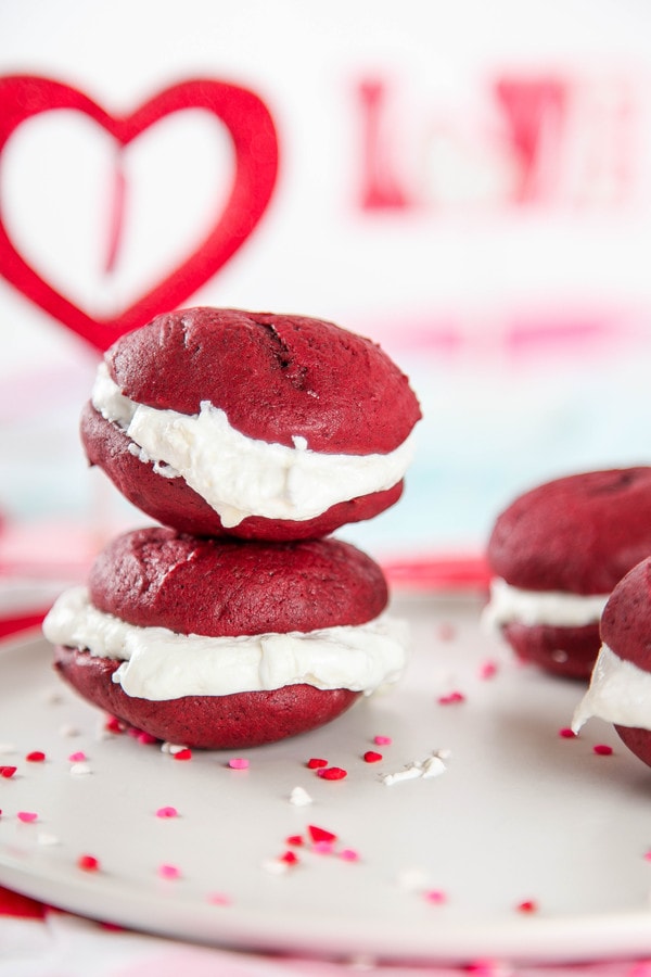 two red velvet whoopie pies with cream cheese marshmallow frosting stacked on top of each other.