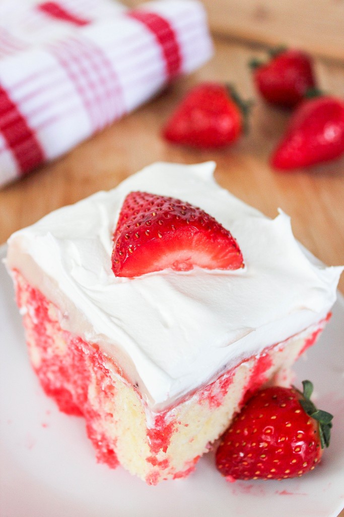 a white cake with strawberry jello stopped with cool whip and a strawberry. 
