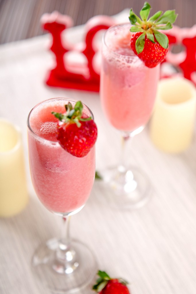 a closeup of a strawberry raspberry mimosa in a champagne glass garnished with a strawberry.