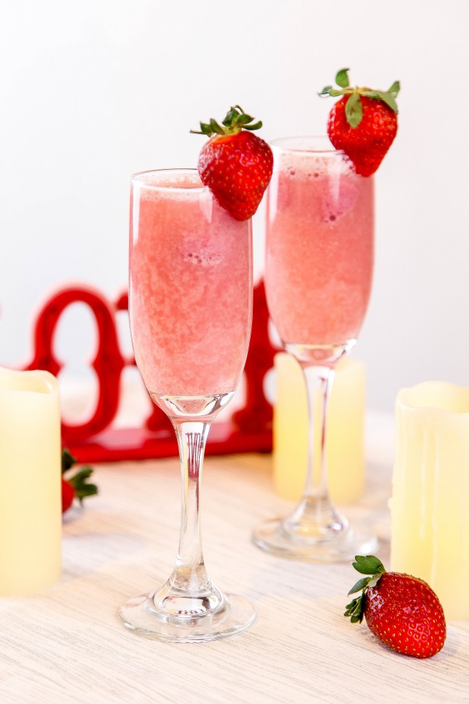 two strawberry mimosas on a table surrounded by candles. 
