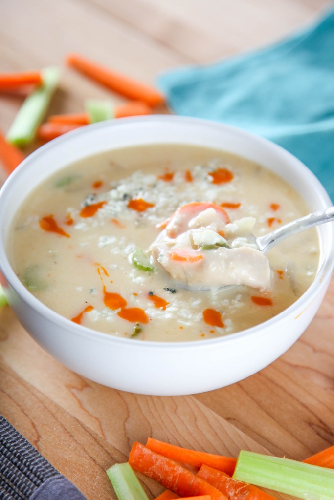 a spoon lifting out a bite of buffalo chicken soup with chicken, carrots, and celery. 
