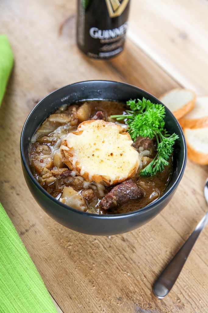 Guinness and beef stew topped with cheesy bread with a bottle of Guinness beer in the background.