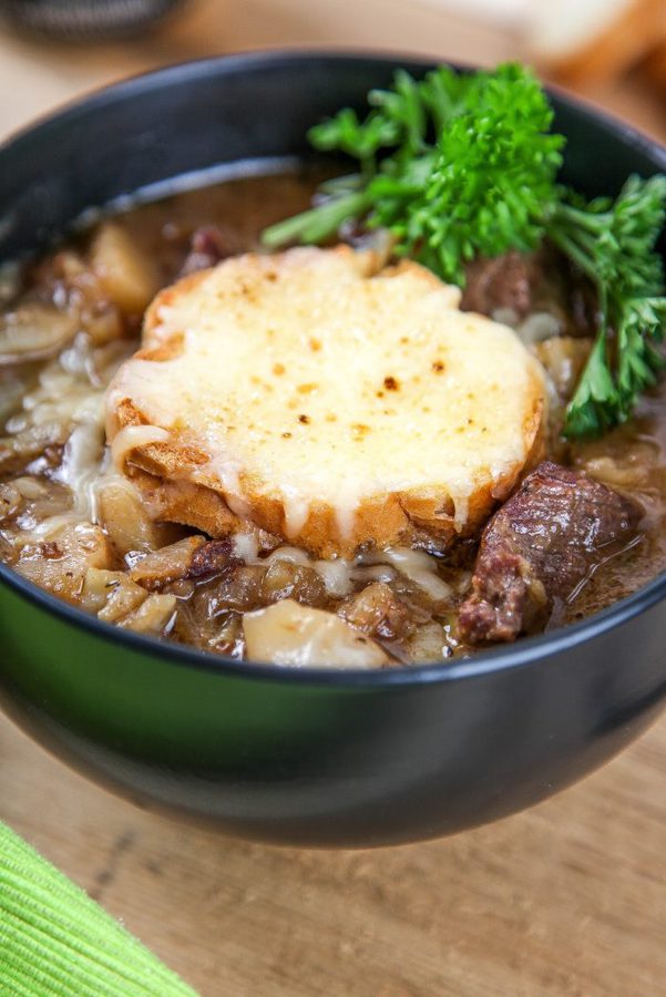 Guinness beef stew topped with a cheesy baguette and parsley in a black bowl.