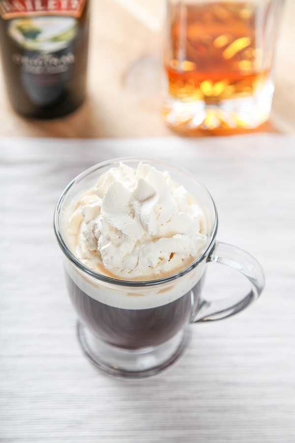 Irish Coffee Recipe in a glass mug with bottles of Jameson and Bailey's in the background.