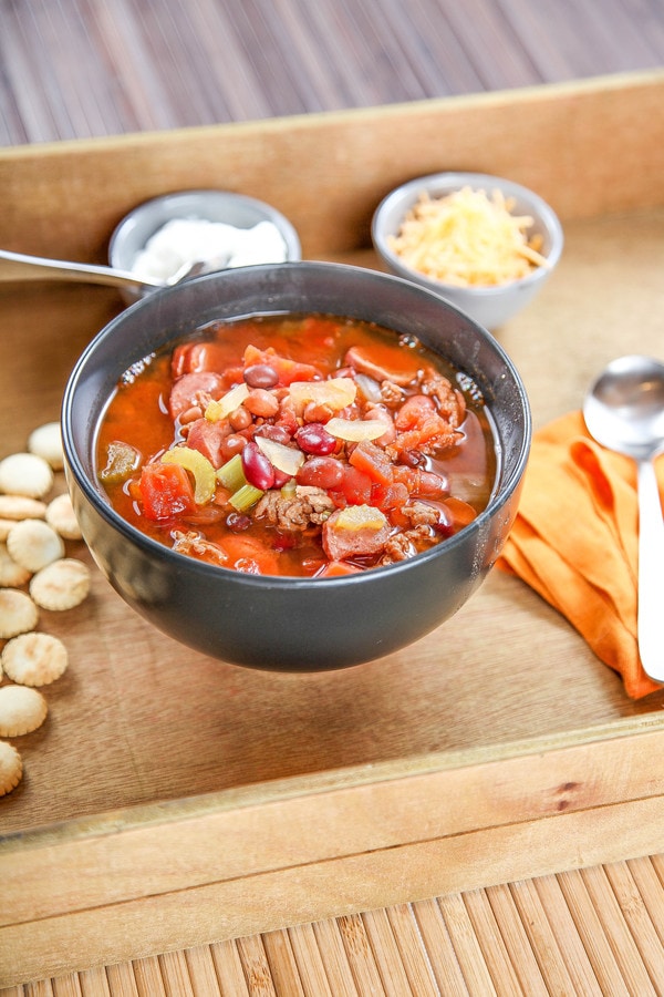 turkey chili with beans, celery, onion, tomatoes, ground turkey, and kielbasa, in a black bowl. 