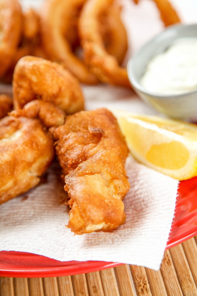 a piece of beer battered cod with a lemon wedge and tartar sauce.