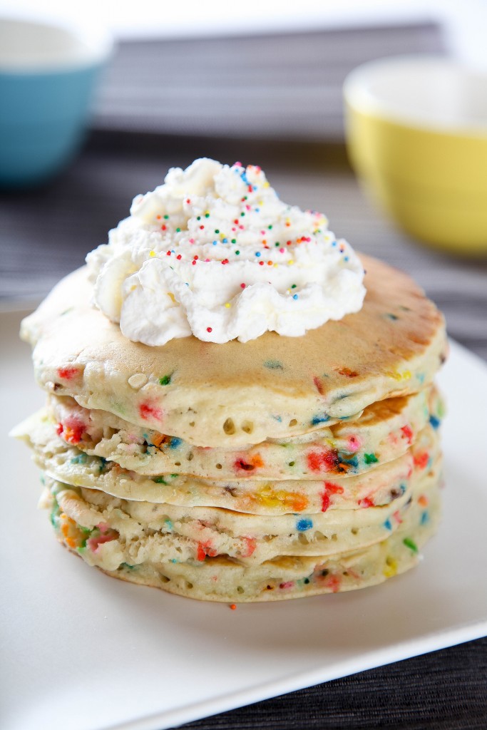 a stack of funfetti pancakes topped with sweetened whipped cream and sprinkles. 