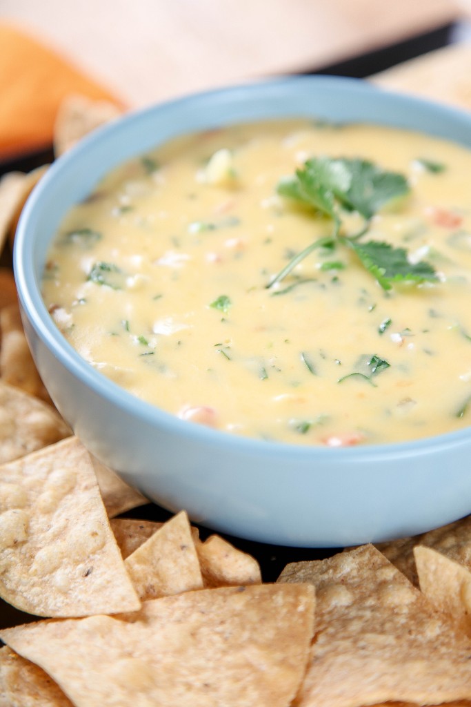 a large blue bowl of chile con queso dip with tomatoes and topped with cilantro. 