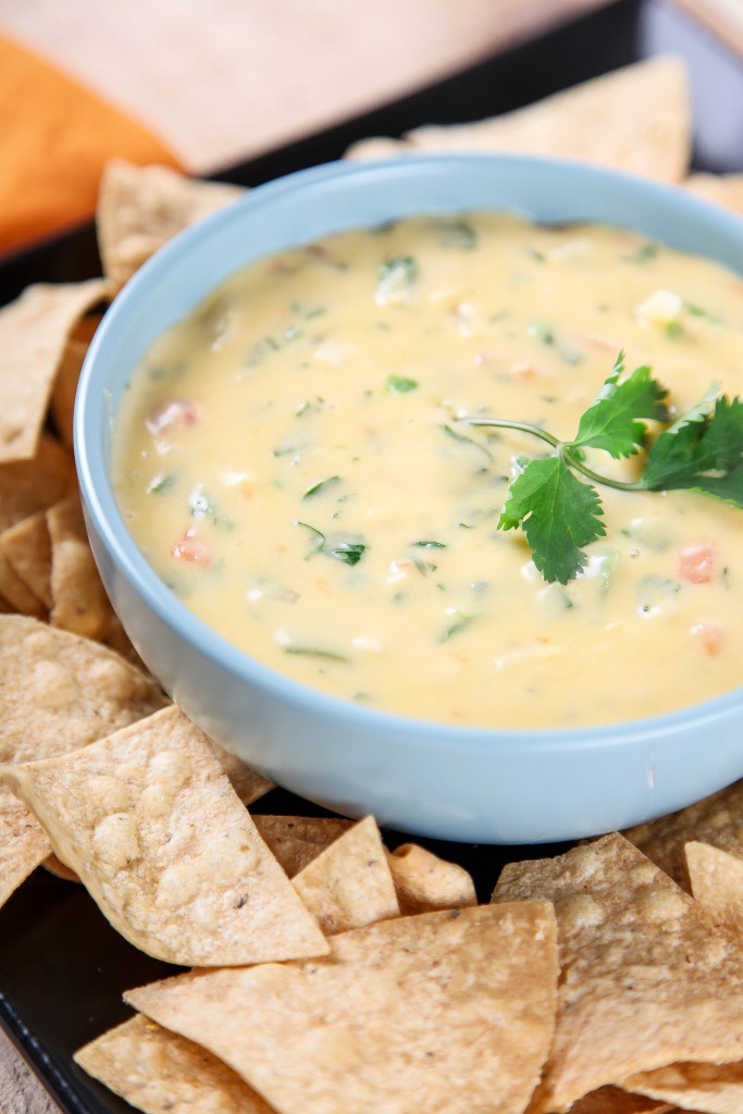 a large blue bowl of cheese dip with peppers, tomatoes, and cilantro. 