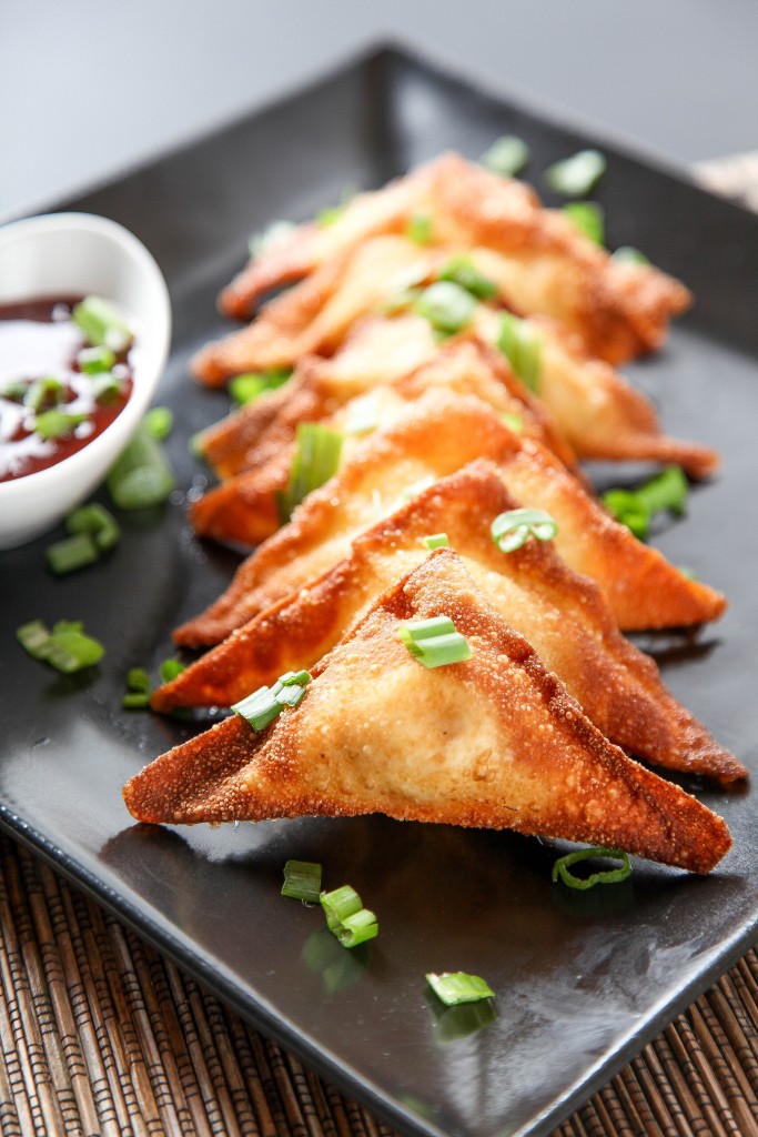 crab and cream cheese wontons on a black plate garnished with green onions. 