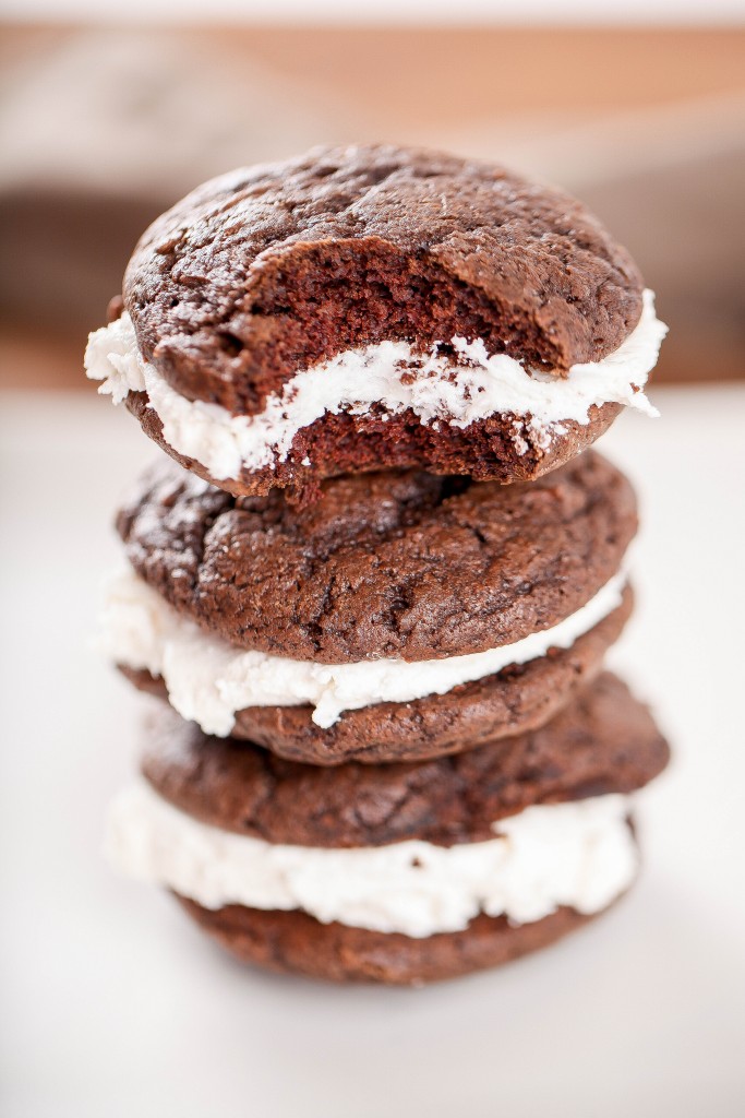 three chocolate whoopie pies with marshmallow frosting stacked on top of each other.