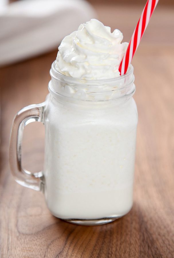 a vanilla frappuccino in a tall glass mug topped with lots of whipped cream on a wooden table. 