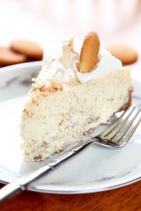 a slice of banana pudding cheesecake topped with whipped cream and a vanilla wafer.