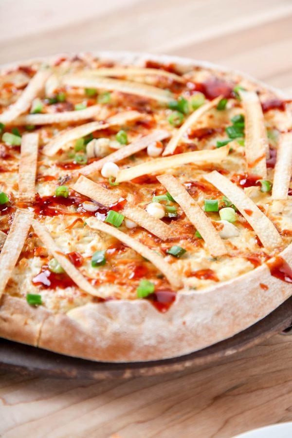 A crab rangoon pizza topped with wonton strips, green onions, and hot sauce.