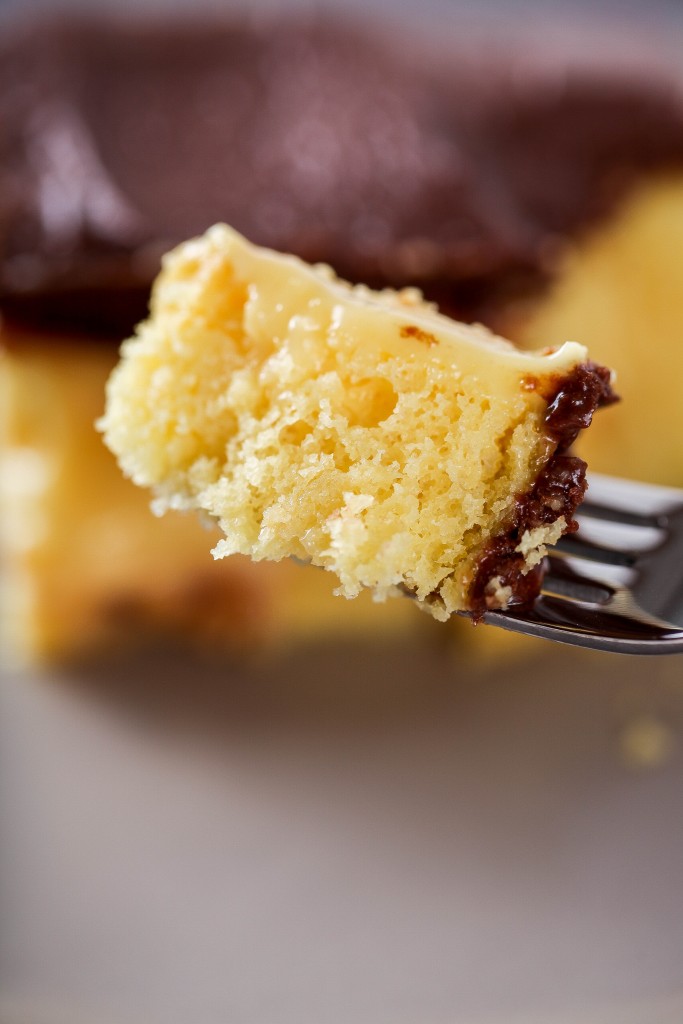 a bite of yellow Boston cream poke cake with chocolate frosting on a metal fork. 