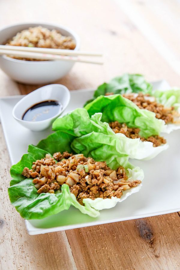 three lettuce leaves filled with a savory ground chicken filling with a dish of soy sauce in the background.