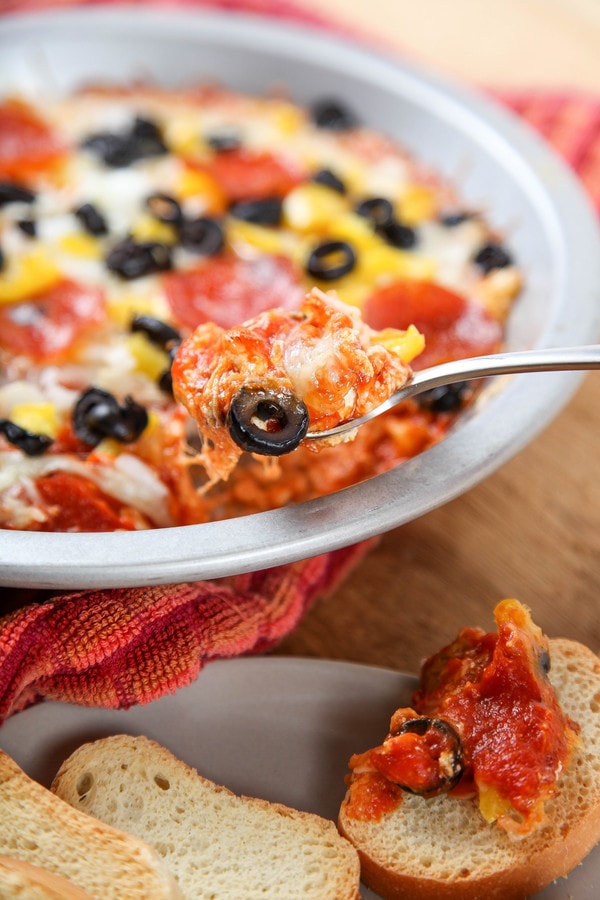 a spoon of pizza dip with yellow bell peppers, cheese, and black olives.