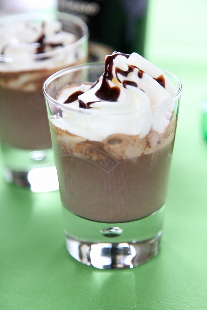 a closeup of bailey's hot chocolate with whipped cream on a green background.