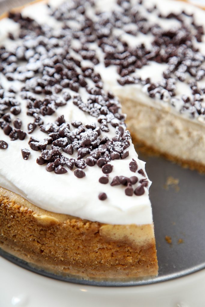 a whole cannoli cheesecake in a graham cracker crust with one slice missing. 