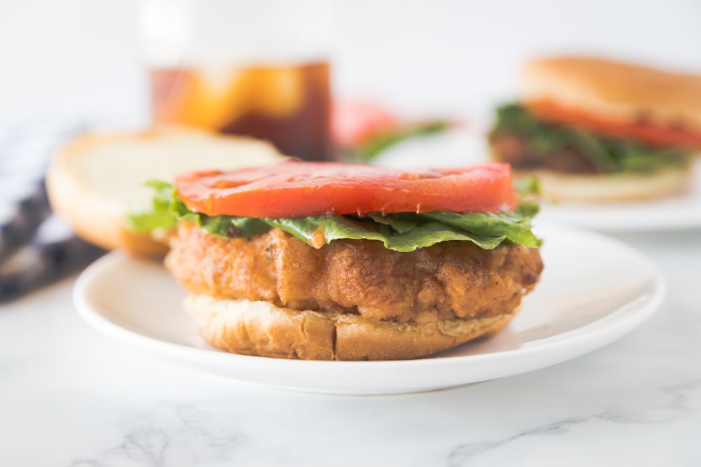 a bun topped with a fried pork chop, lettuce, and tomato