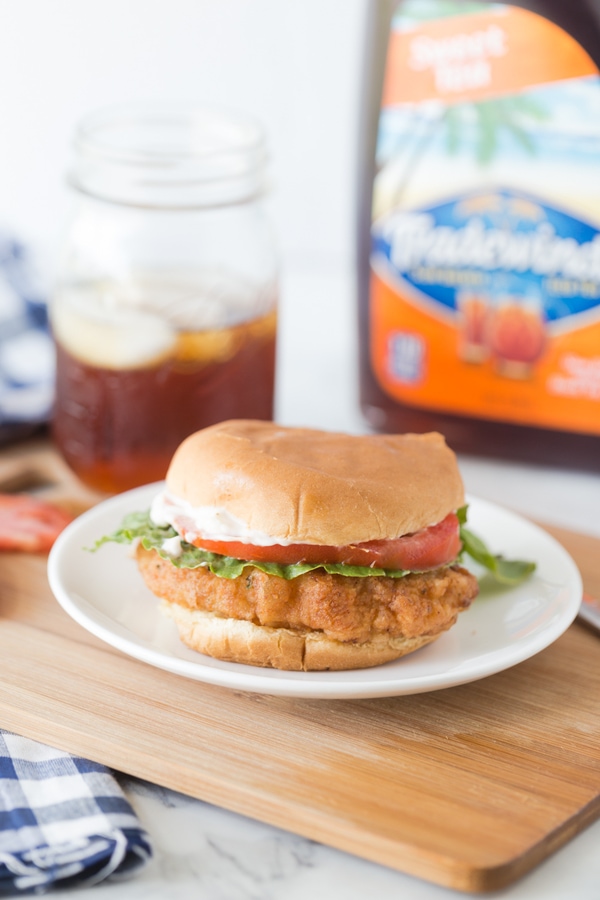 a fried pork chop sandwich on a bun with lettuce, tomato, and mayonnaise.