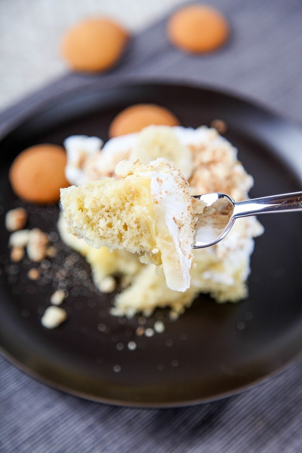 a bite of banana pudding poke cake on a fork with the cake below on a black plate.