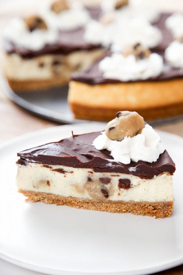 a sideways slice of cookie dough cheesecake topped with chocolate ganache, whipped cream,and cookie dough.