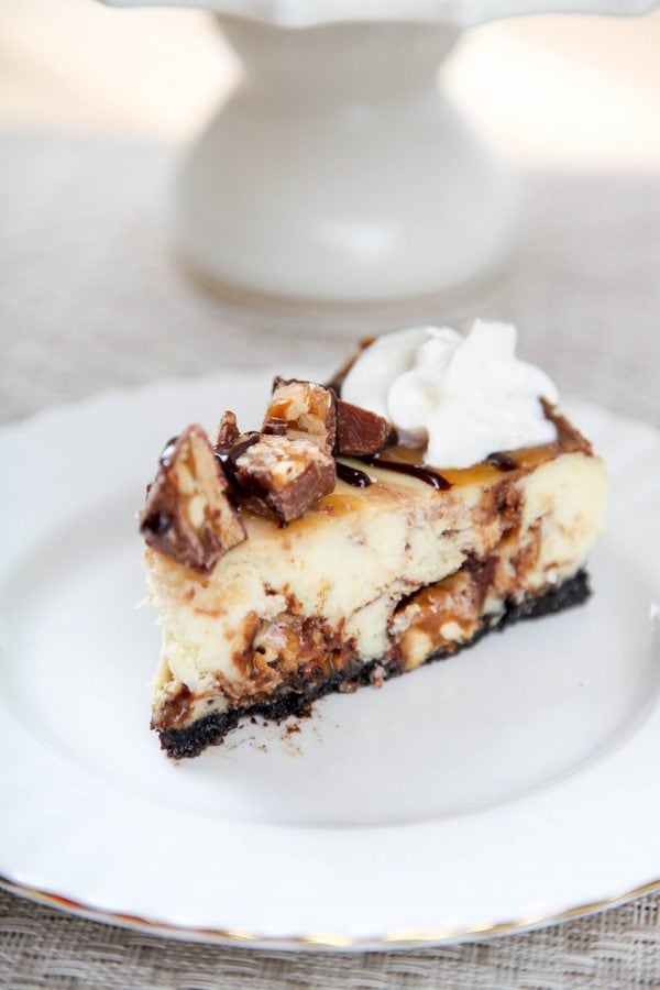 a slice of snickers cheesecake topped with whipped cream, chocolate sauce, and caramel. 