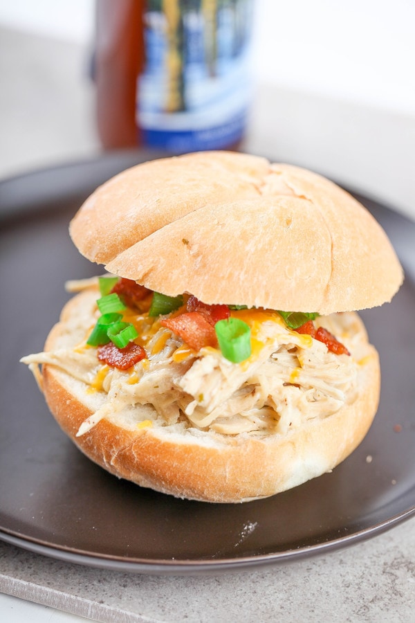 a sandwich with cream chicken, bacon, cheese, and green onions on a black plate. 