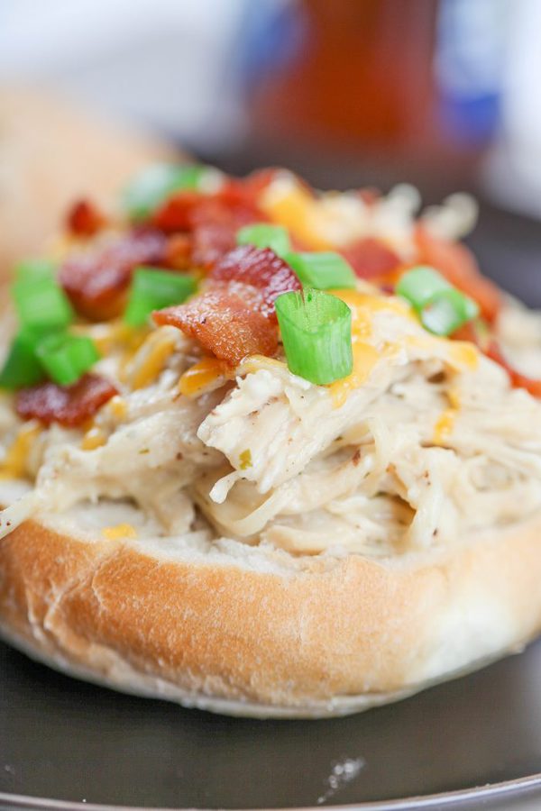 a closeup of shredded ranch chicken topped with cheddar cheese, bacon, and green onions.