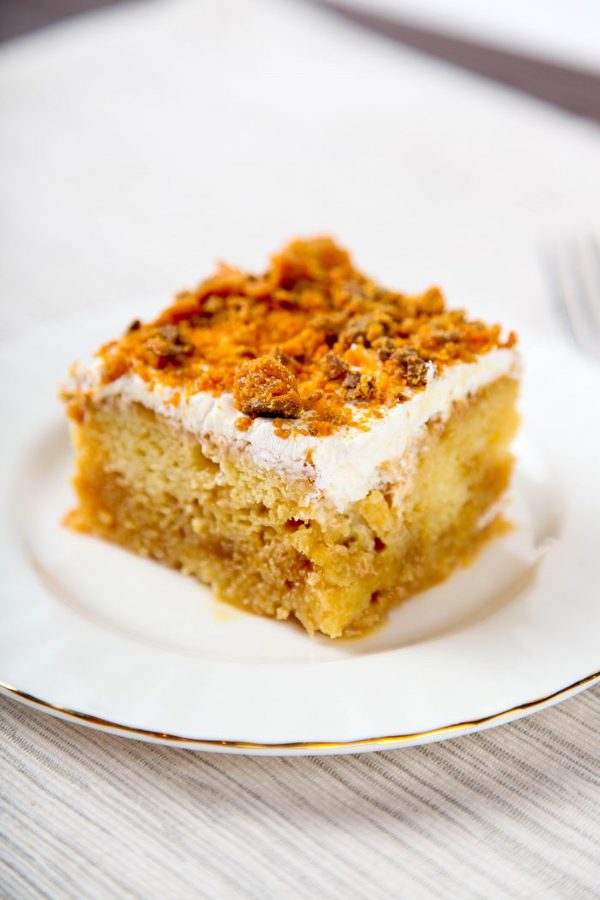 one slice of caramel poke cake topped with butterfingers on a white plate.