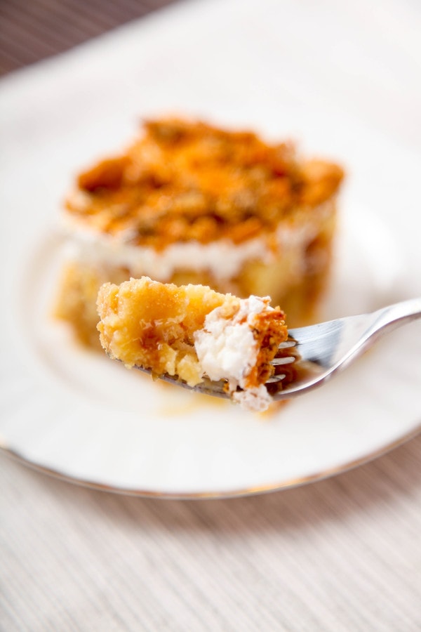 a closeup of one bite of butterfinger cake on a fork with a slice of cake in the background.