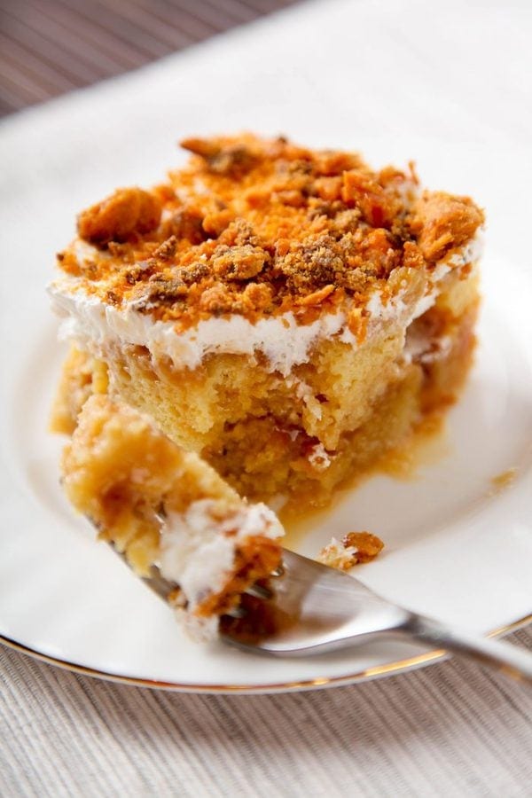 a slice of butterfinger poke cake with one bite taken out of it.