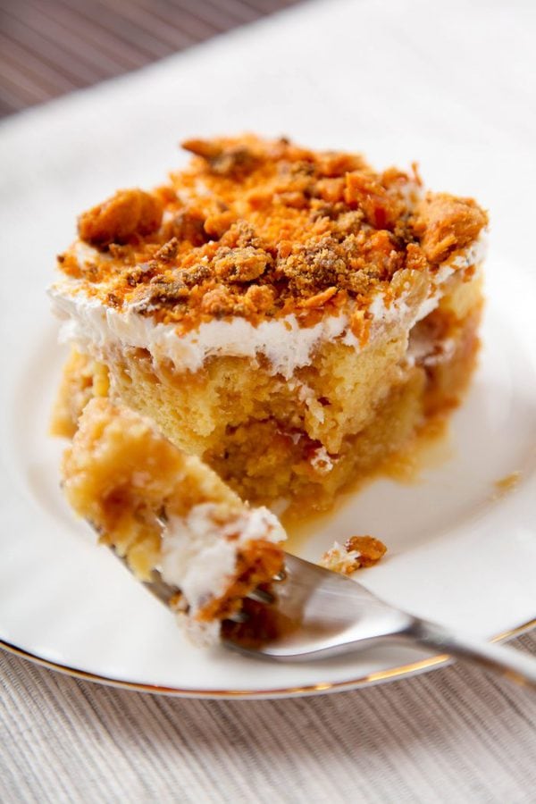 a slice of butterfinger poke cake with one bite taken out of it. 